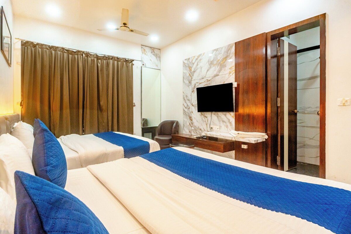 Habitación de hotel con dos camas, un baño con espejo y un televisor en la pared.