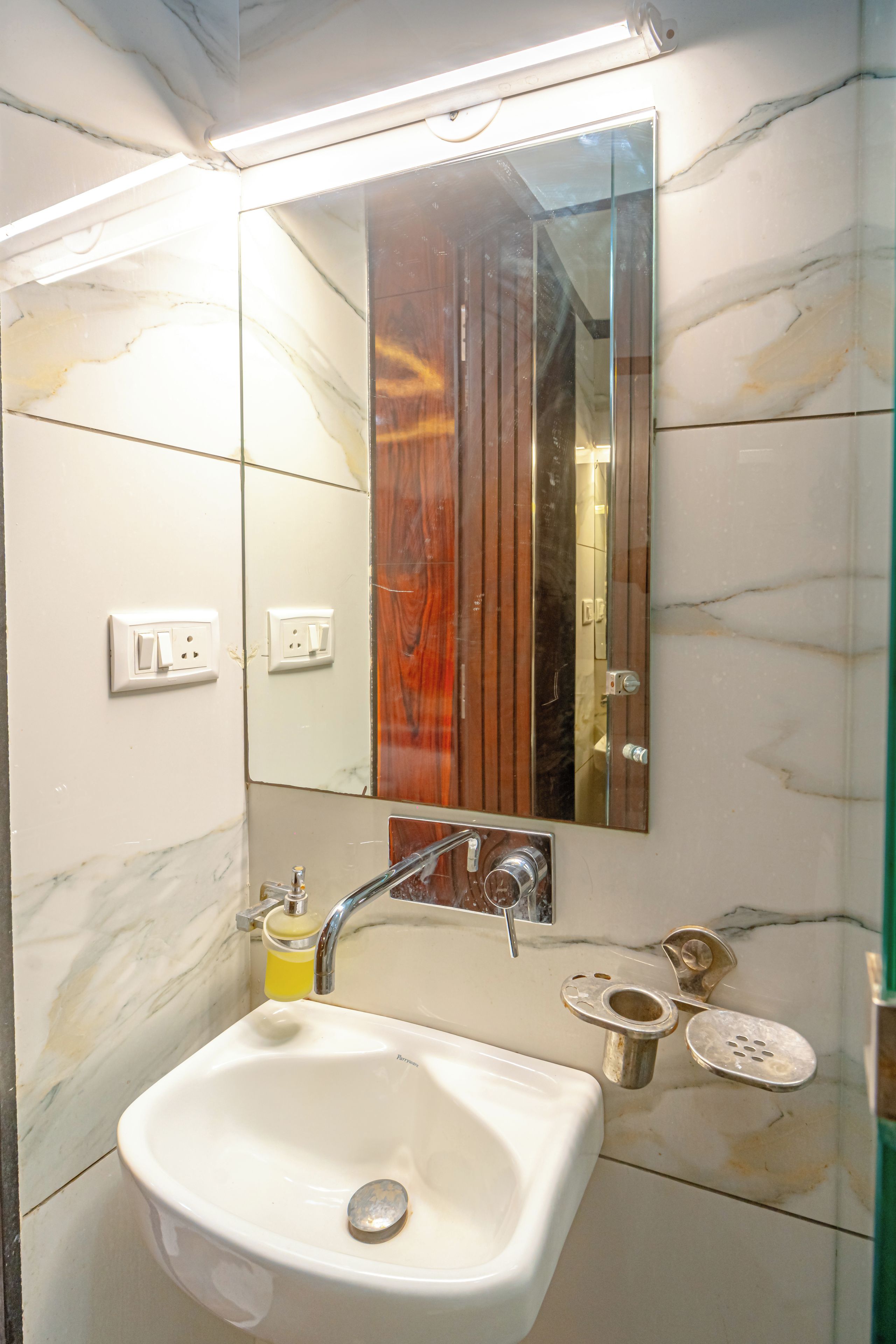 A bathroom with a white sink, a mirror, and a wooden panel.