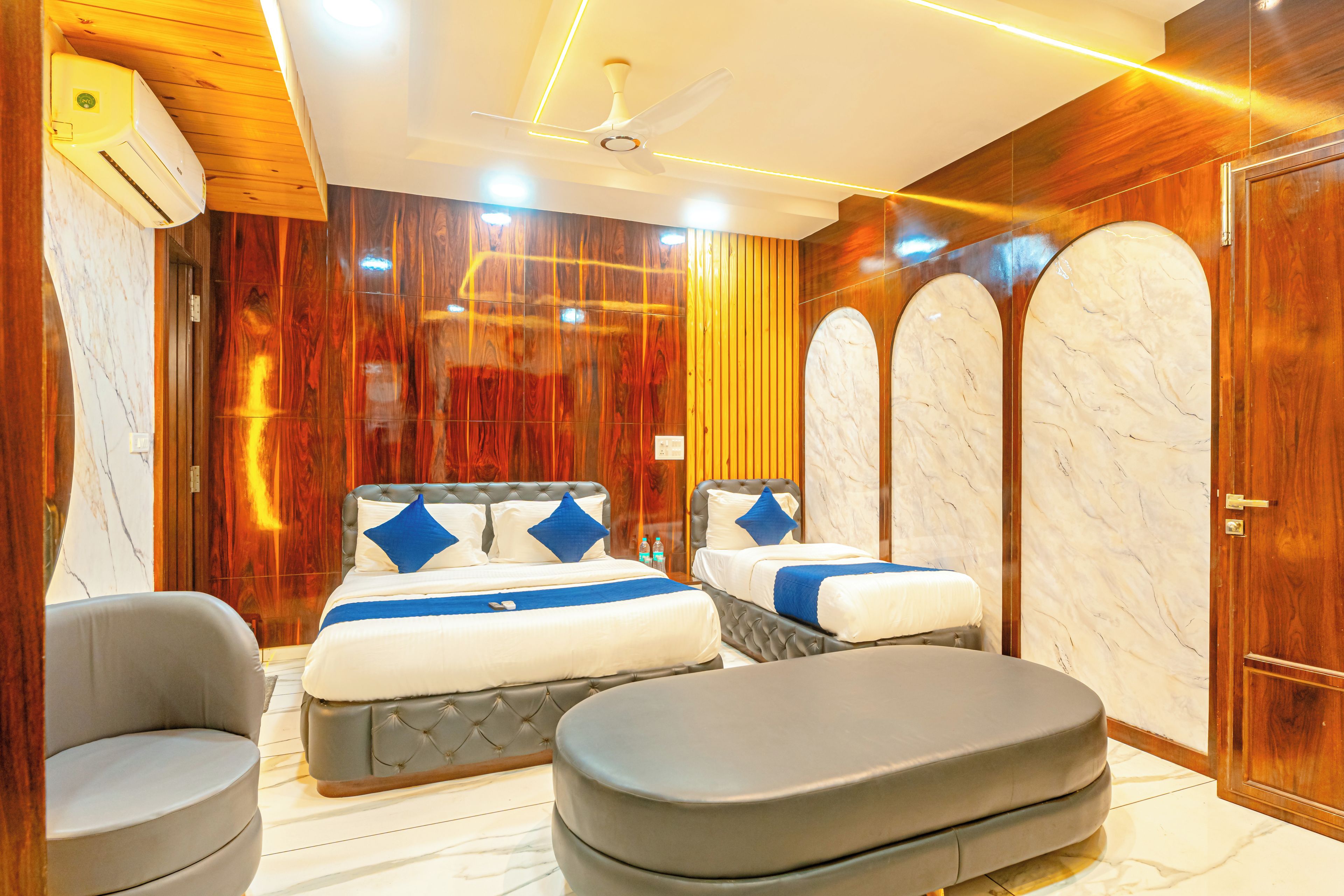 A hotel room with a large bed, two smaller beds, a seating area, and a wooden wall with a marble accent.