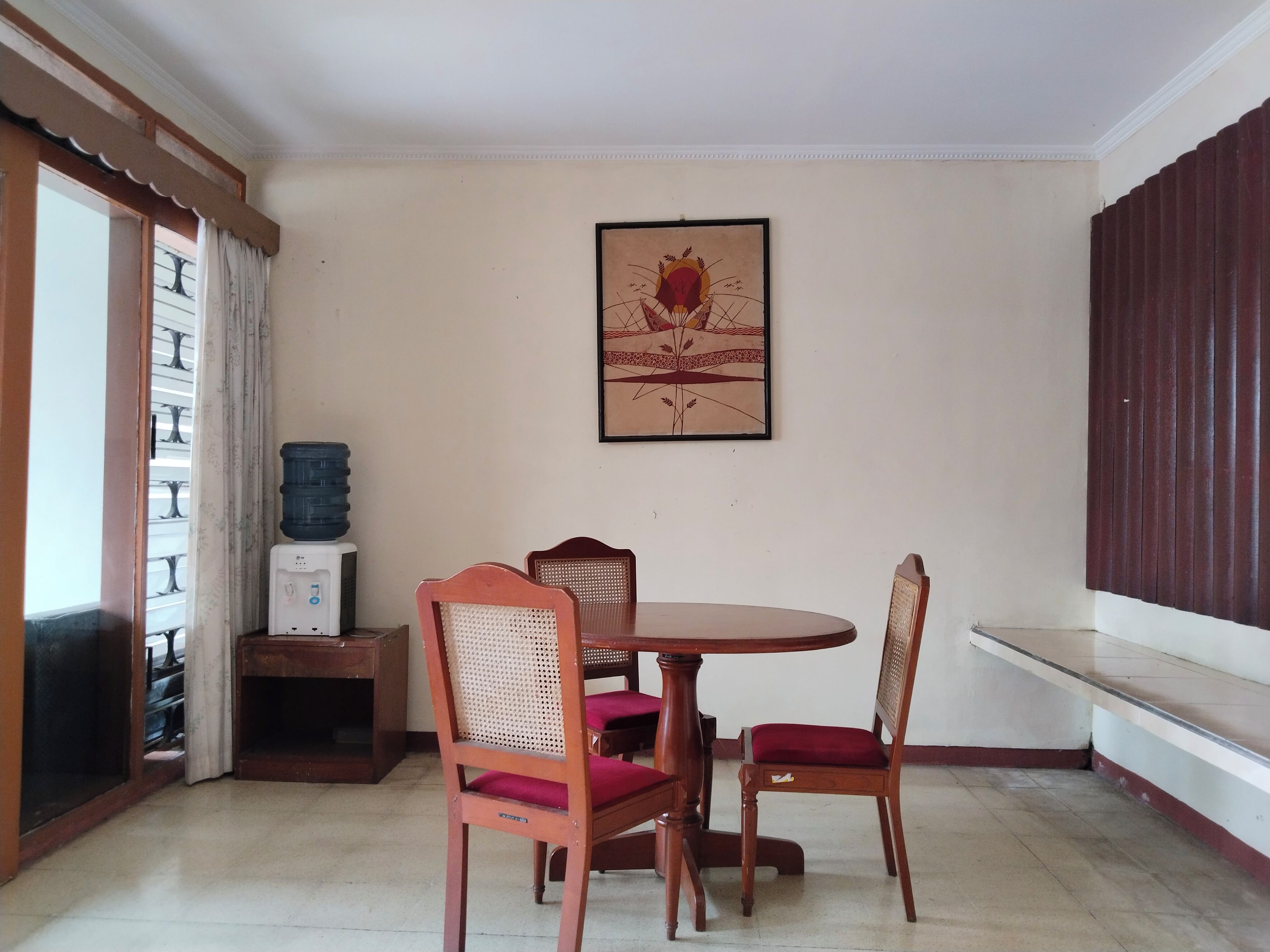 Un comedor con una mesa redonda y cuatro sillas, un dispensador de agua y una obra de arte enmarcada en la pared.