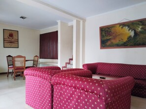 A living room with a red patterned sofa set, a dining table with chairs, and a painting on the wall.
