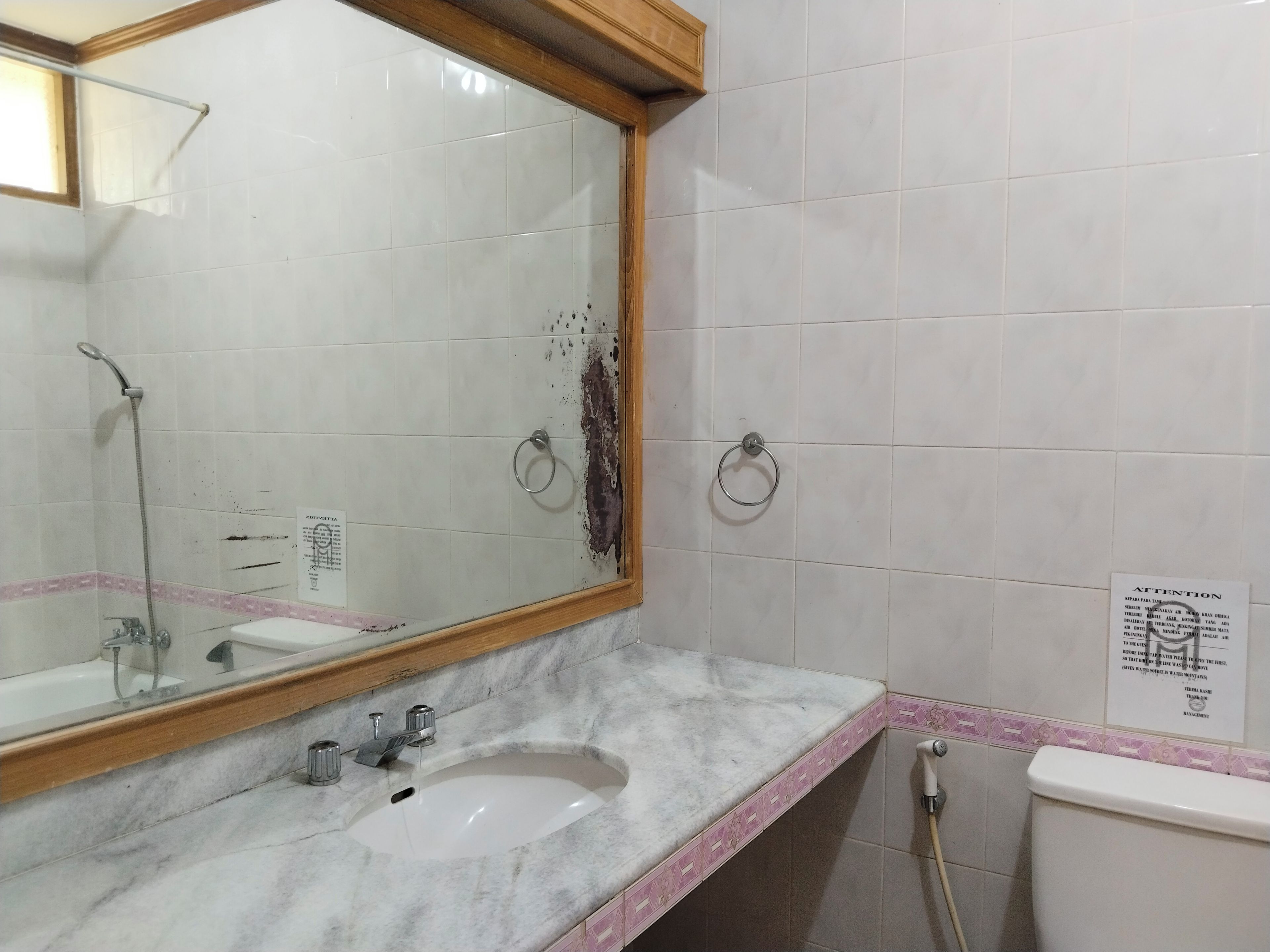 A bathroom with a sink, mirror, and towel rings.