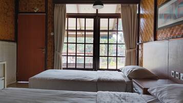 Una habitación con dos camas, techo de madera, ventana con cortinas y una puerta.