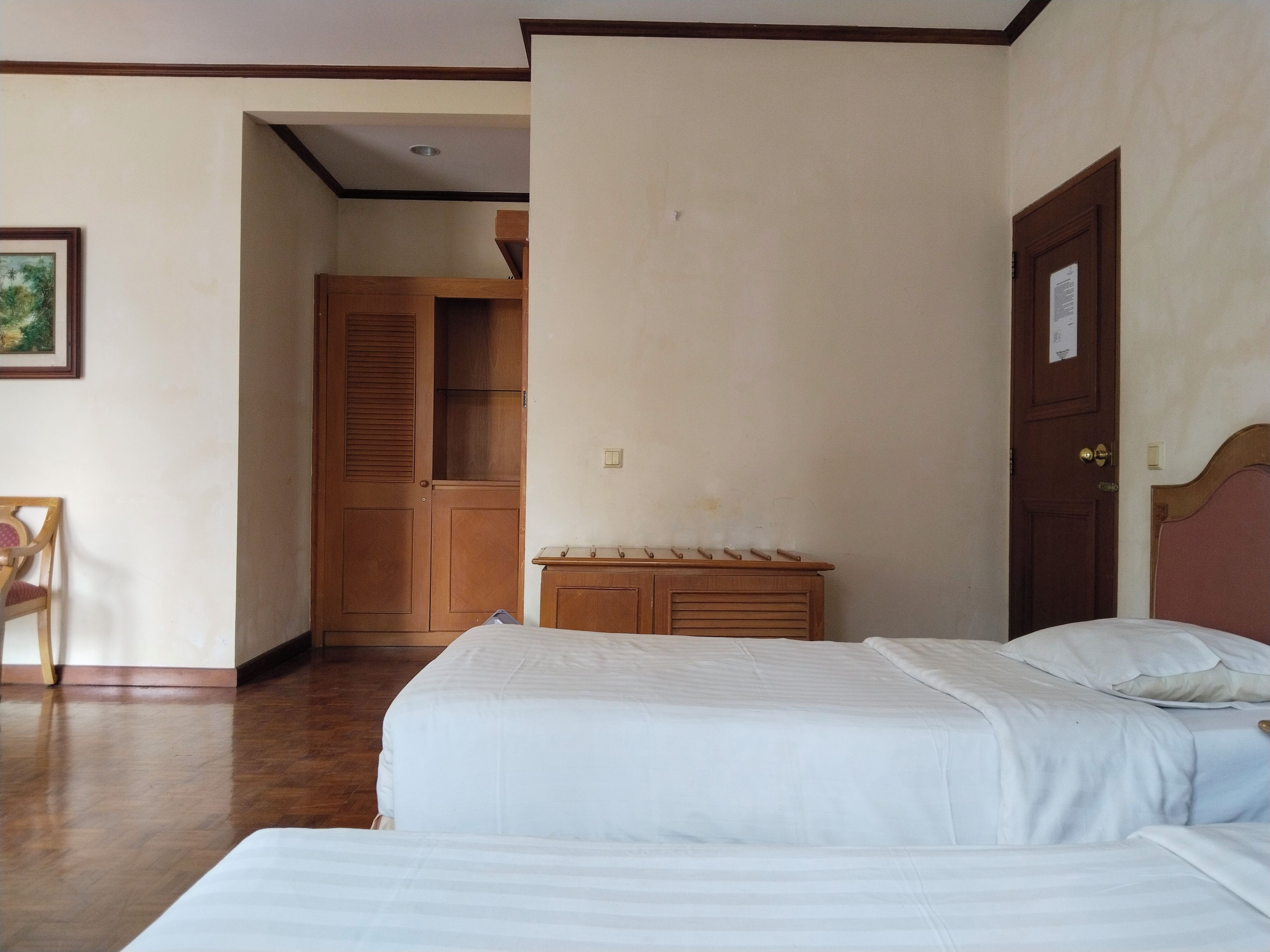 A hotel room with two beds, a wooden wardrobe, a small table, and a chair.