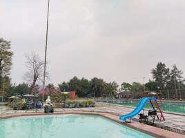 Una piscina con un tobogán azul, rodeada de sillas de descanso y sombrillas.