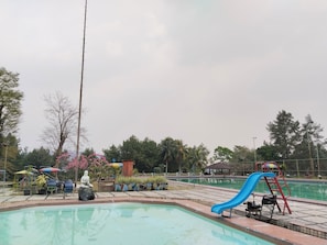 Une piscine avec un toboggan bleu, entourée de chaises longues et de parasols.