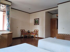 Habitación de hotel con dos camas, un escritorio de madera, una silla, una mesita con una tetera y un cuadro en la pared.