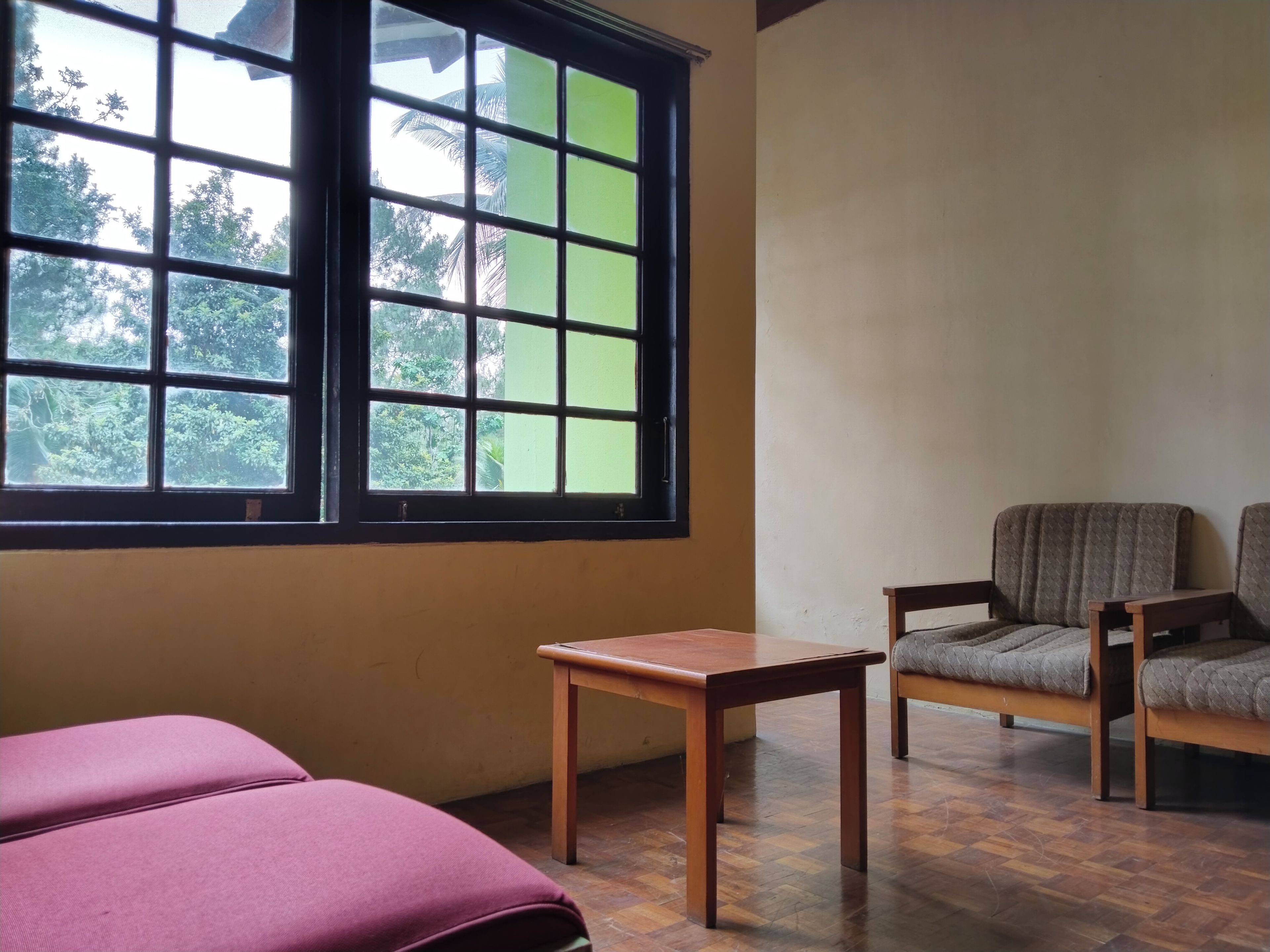 Een kamer met een groot raam, een houten tafel, twee fauteuils en een bed.
