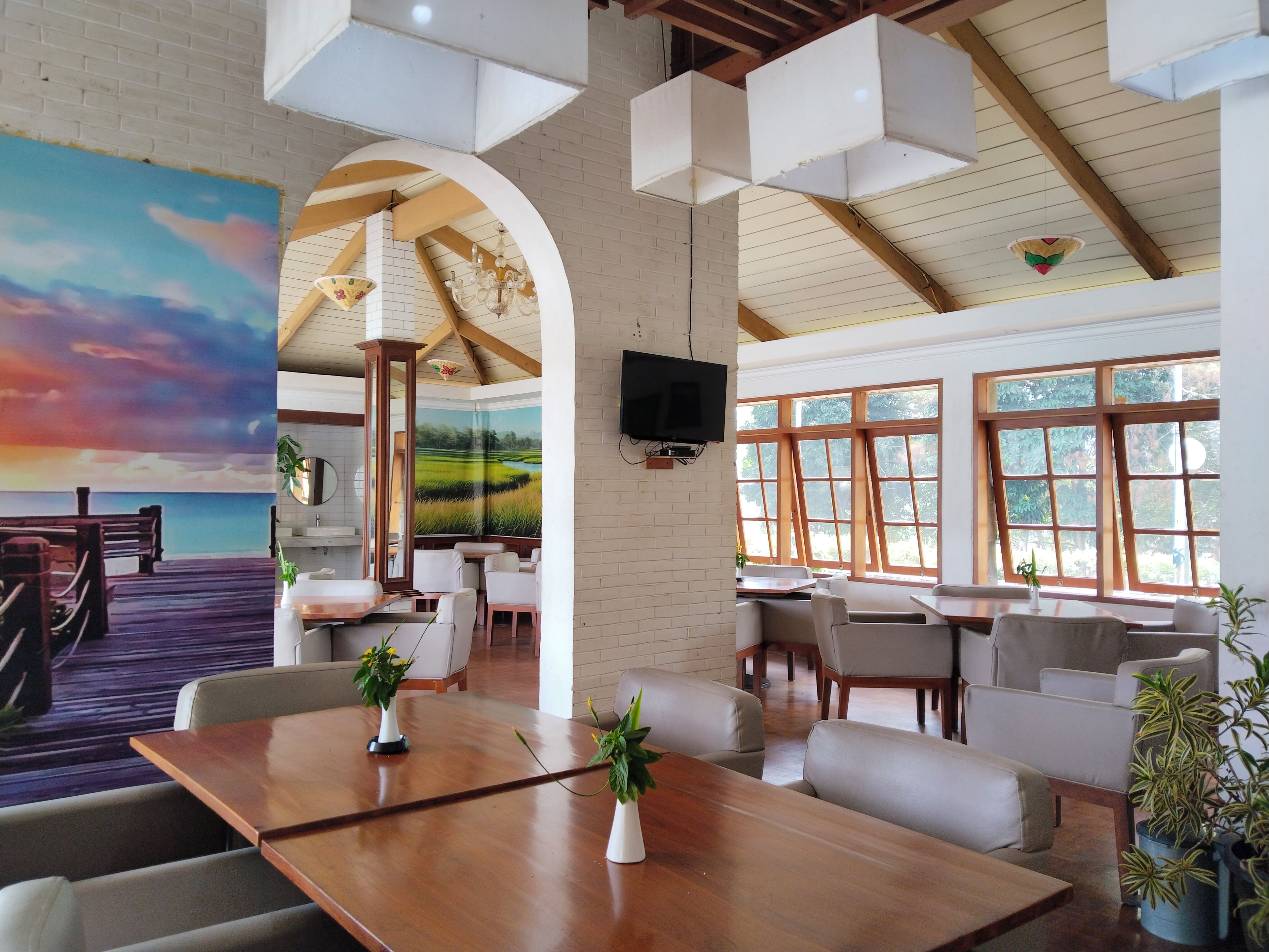 Un restaurante con terraza de madera, paredes blancas y amplios ventanales.
