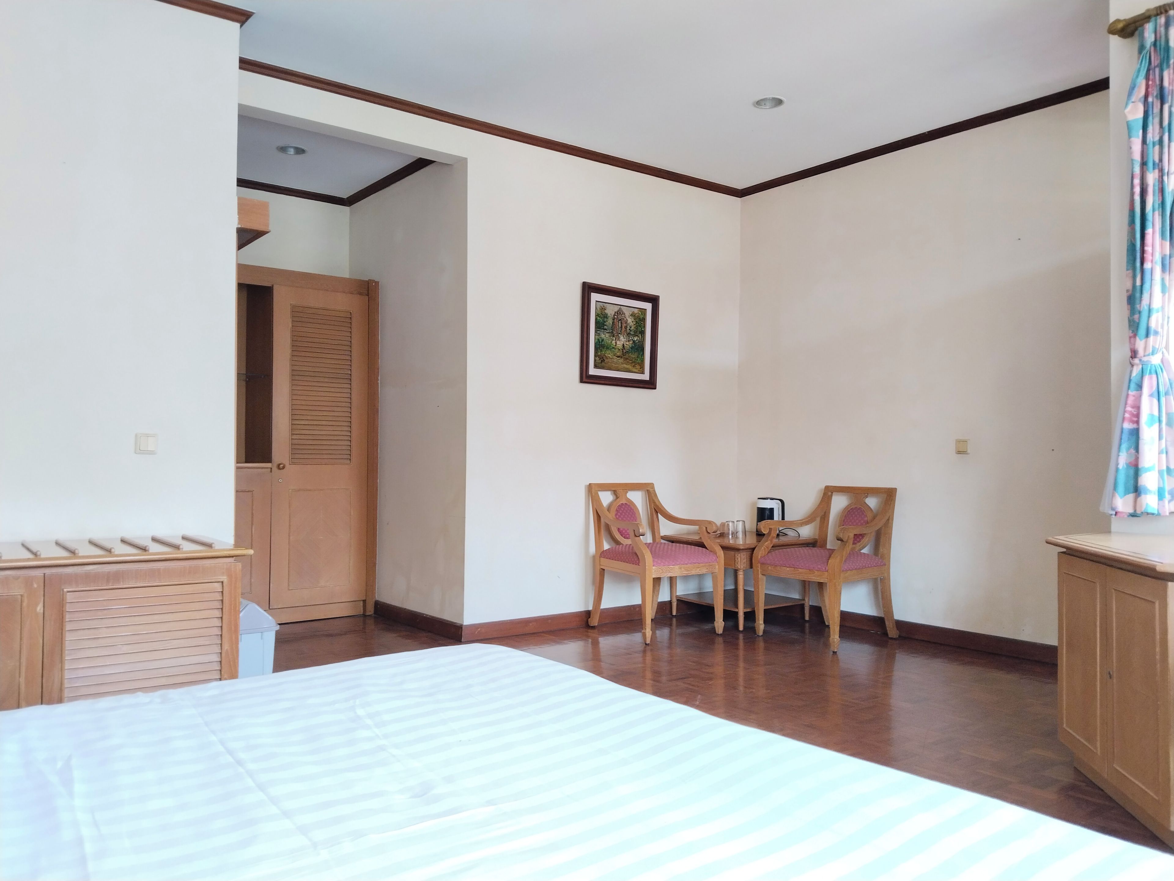 Una habitación con una cama, un armario de madera, una mesita con sillas y un cuadro en la pared.