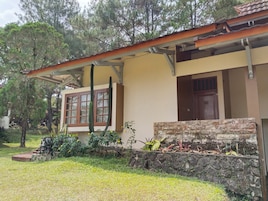 Un edificio con un muro de contención de piedra, una ventana con marco marrón y una puerta con placa numérica.
