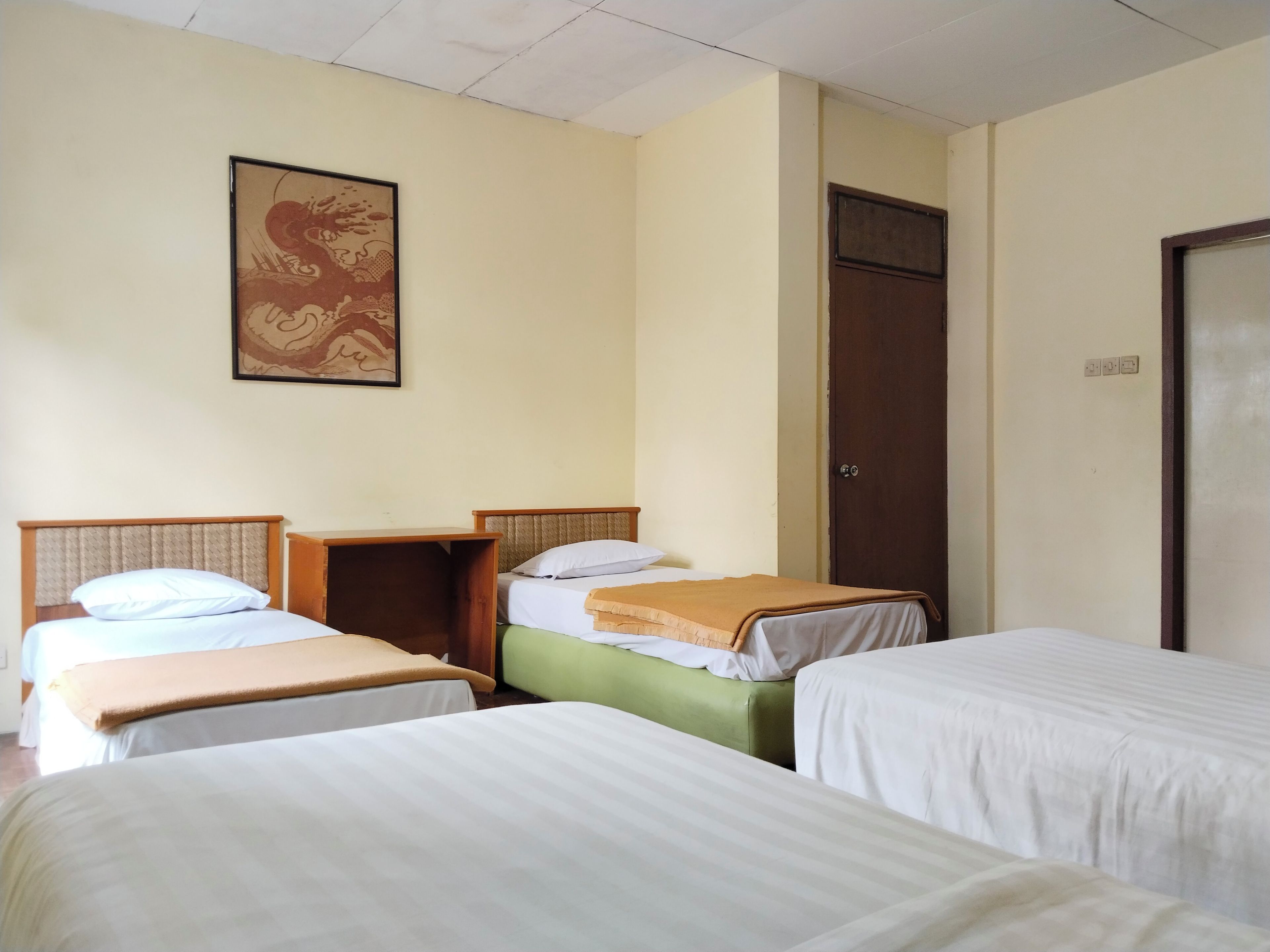 A room with three beds arranged in a row, a wooden headboard, a wall-mounted artwork, and a door with a handle.