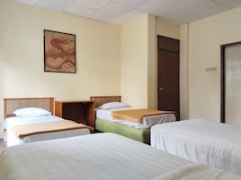 Una habitación con tres camas dispuestas en fila, un cabecero de madera, una obra de arte en la pared y una puerta con manija.