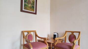 A corner room with two wooden chairs with cushioned seats, a small table, a framed picture on the wall, and a coffee maker on the table.