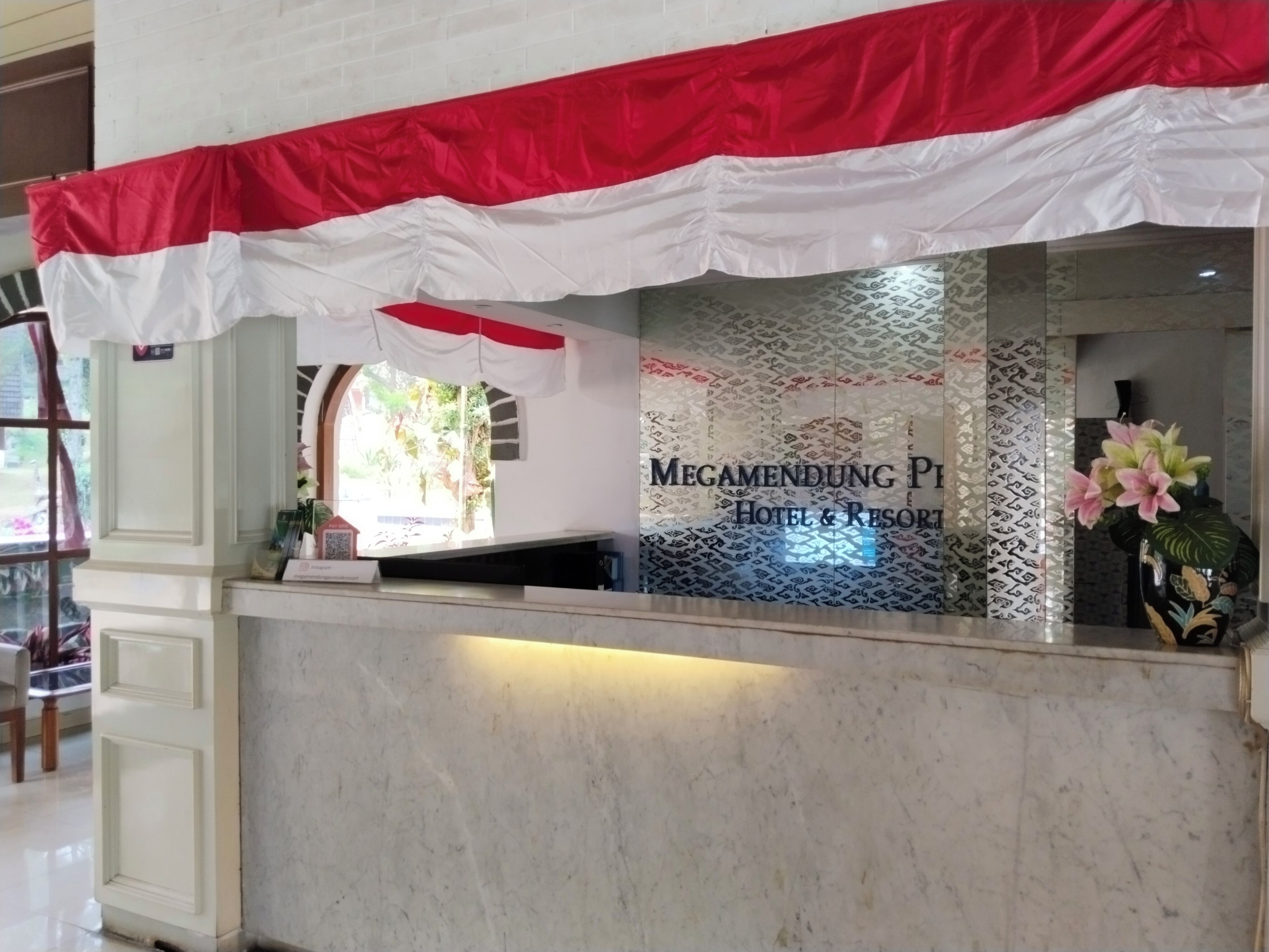 A reception desk with a red and white striped awning, a sign reading 'Megamendung P1 Hotel & Resort', and a vase with flowers.