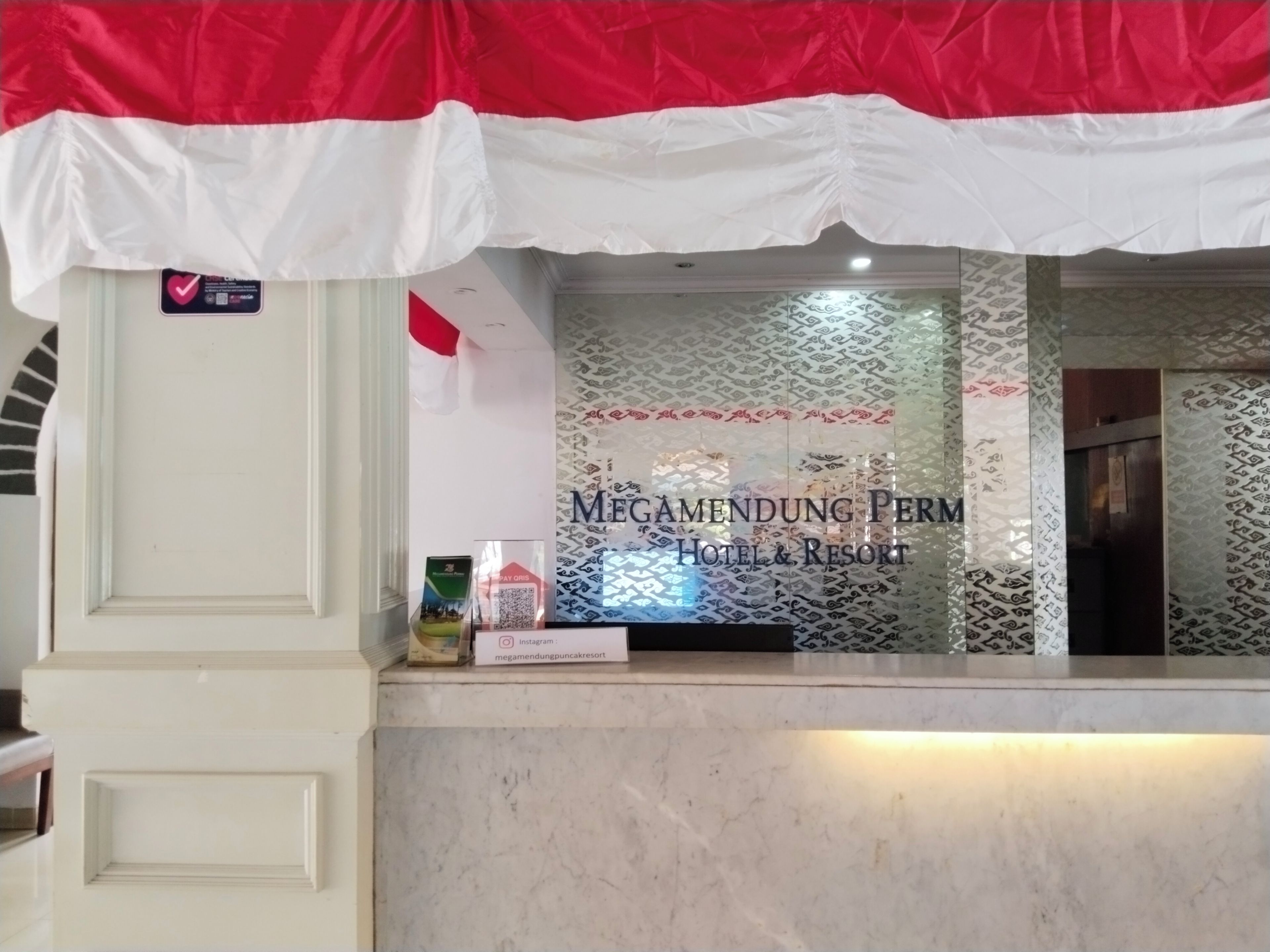 A reception desk with a sign for 'MEGAMENDUNG PERM HOTEL & RESORT' and a QR code.