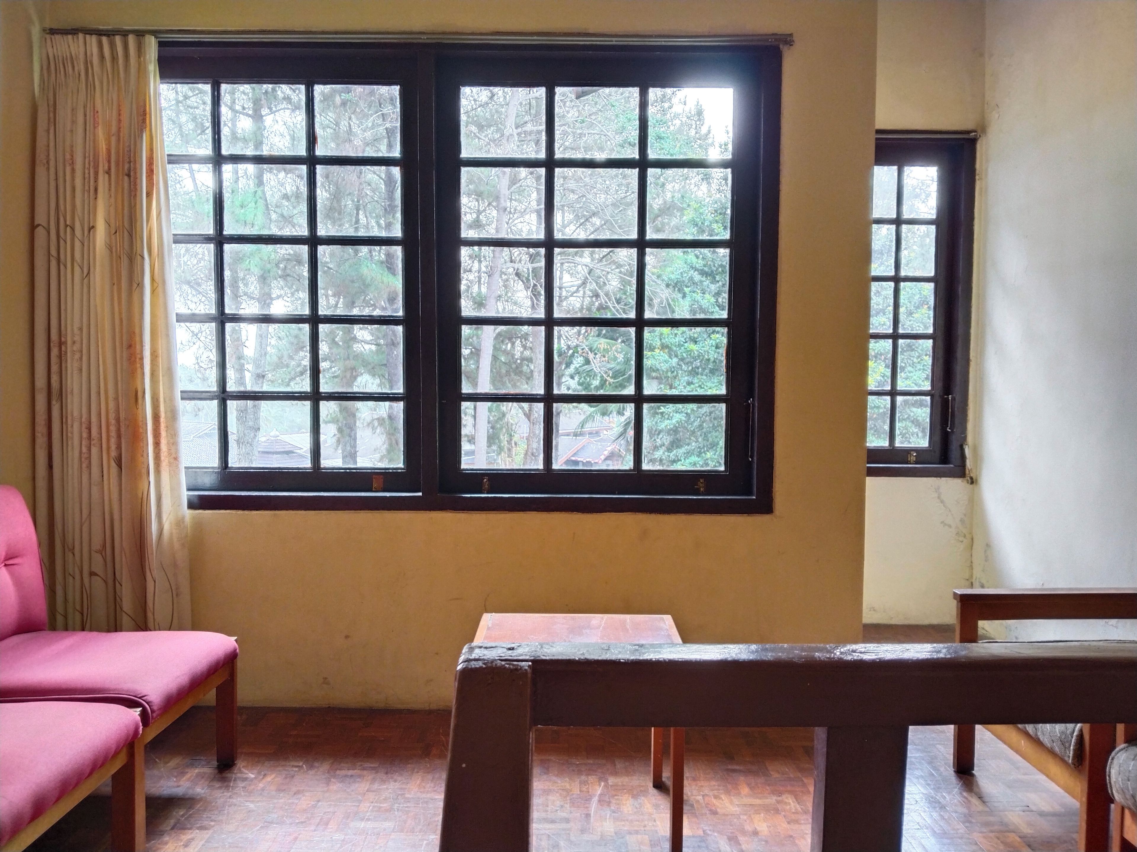 A room with a large window, a wooden bench, and a pink chair.
