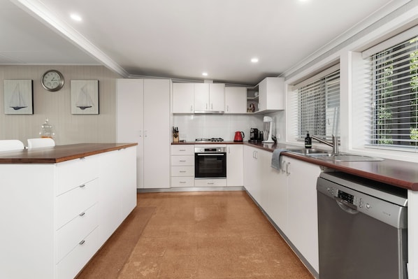 Een moderne keuken met witte kastjes, een houten aanrecht, een ingebouwde oven, een vaatwasser en een raam met zonwering.
