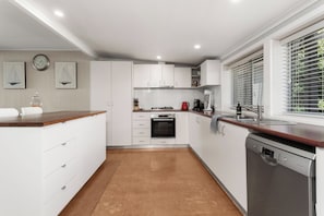 Eine moderne Küche mit weißen Schränken, einer Holz Arbeitsplatte, einem eingebauten Backofen, einem Geschirrspüler und einem Fenster mit Jalousien.