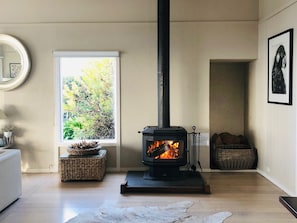 Een kamer met een houtkachel, een raam met uitzicht op bomen en een witte bank.