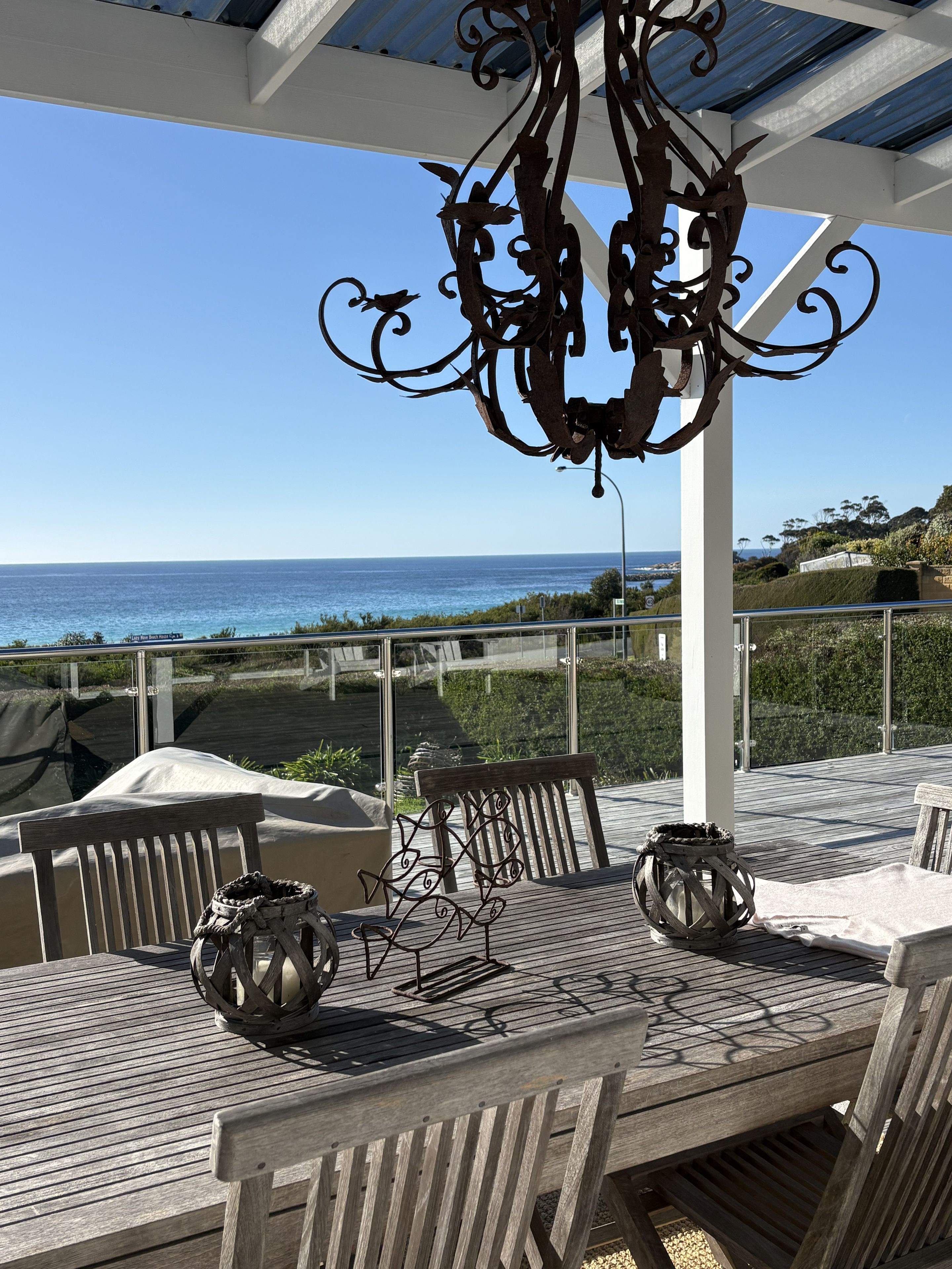 A wooden deck with outdoor seating, a decorative metal chandelier, and a view of the ocean.