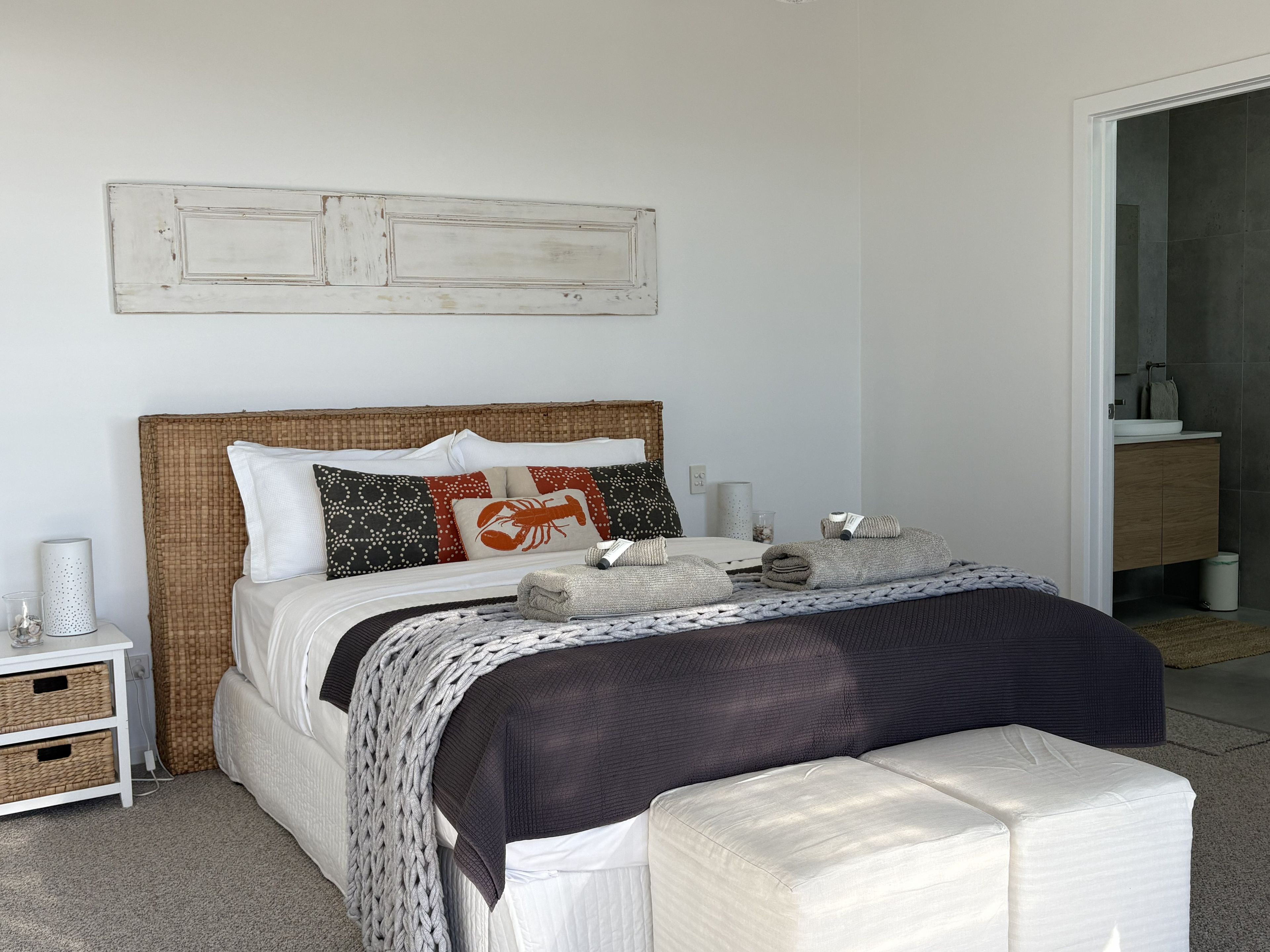 A neatly arranged bedroom with a bed, bedside tables, and a visible bathroom.