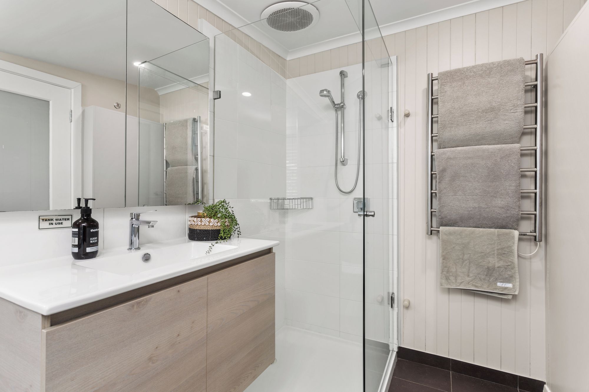 A modern bathroom with a glass shower enclosure, a wooden vanity, and a towel rack with multiple towels.