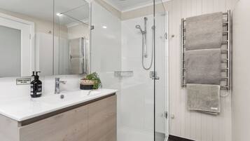 A modern bathroom with a glass shower enclosure, a wooden vanity, and a towel rack with multiple towels.