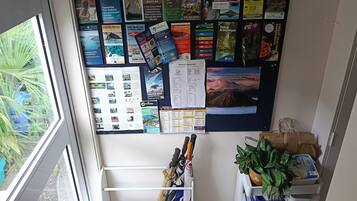 Un panneau d’affichage où sont accrochées des brochures de voyage, avec vue sur la verdure par la fenêtre.
