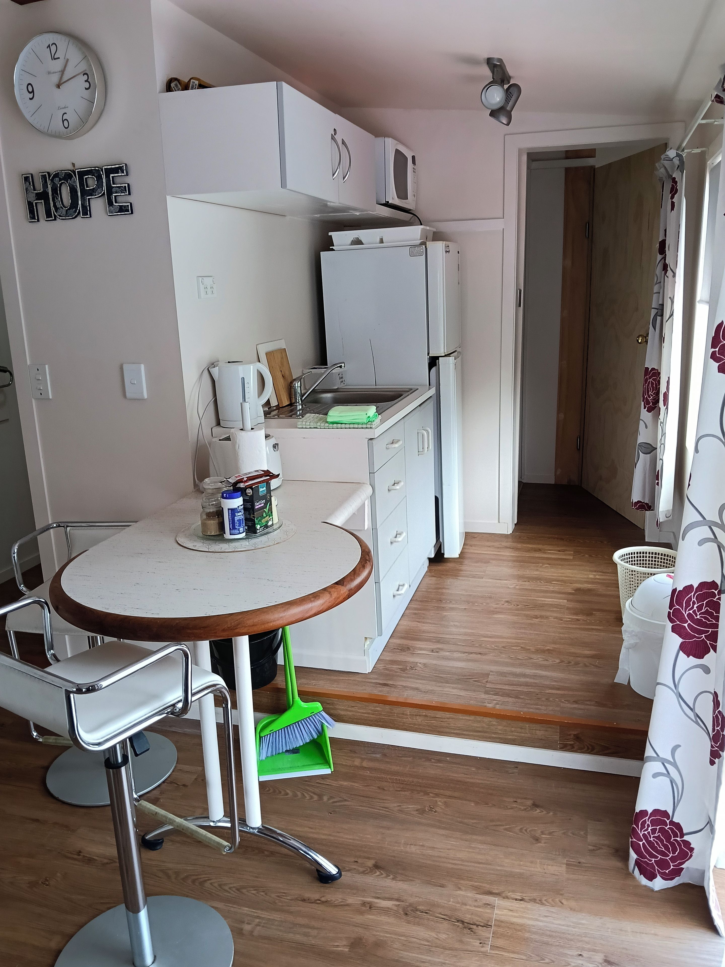 A compact kitchen with a microwave, refrigerator, and a sink. There is a clock on the wall and a sign with the word 'HOPE'.