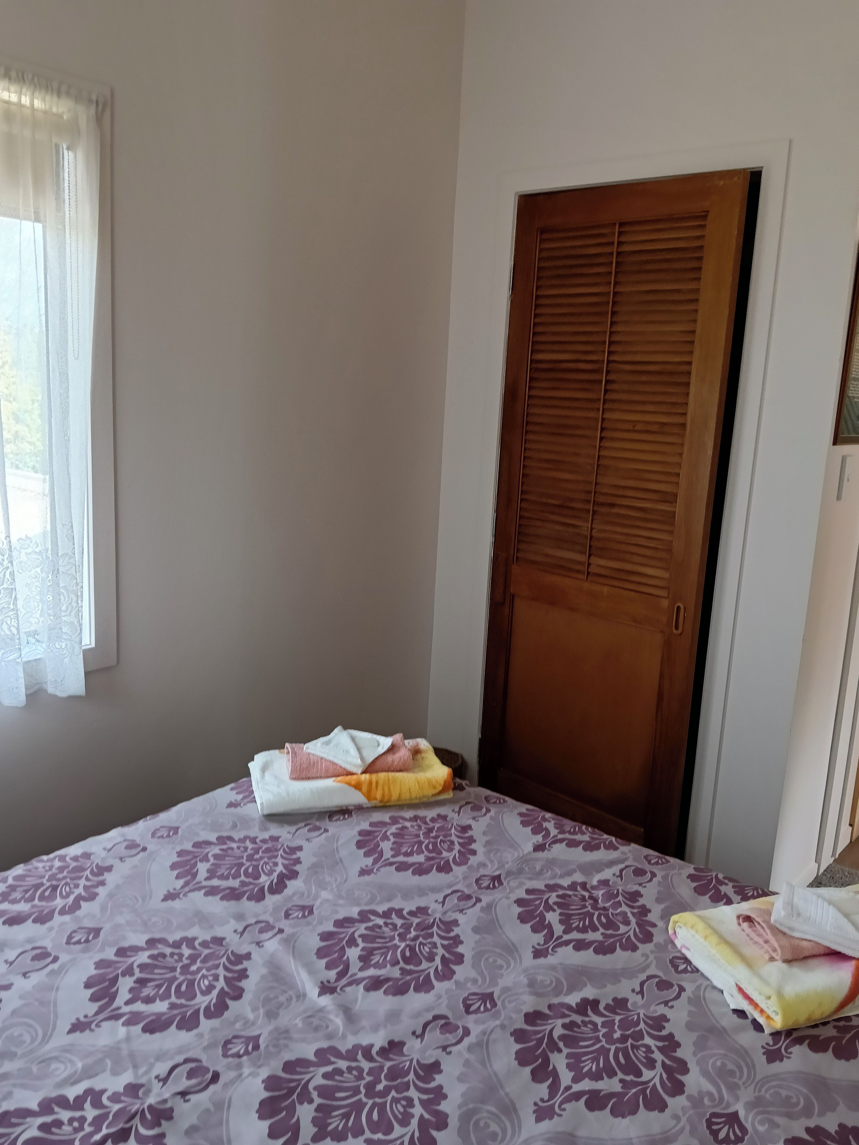 A room with a bed, a wooden door, and a window with sheer curtains.