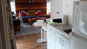 A compact kitchen with white cabinets, a stainless steel refrigerator, and a small dining area with a wooden table and chairs. - Water Brook 2 B/R Studio Apt (Hamilton)