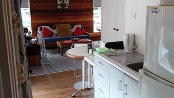 A compact kitchen with white cabinets, a stainless steel refrigerator, and a small dining area with a wooden table and chairs.