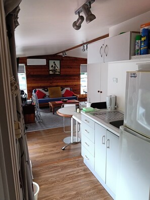 A compact kitchen with white cabinets, a stainless steel refrigerator, and a small dining area with a wooden table and chairs. - Water Brook 2 B/R Studio Apt (Hamilton)