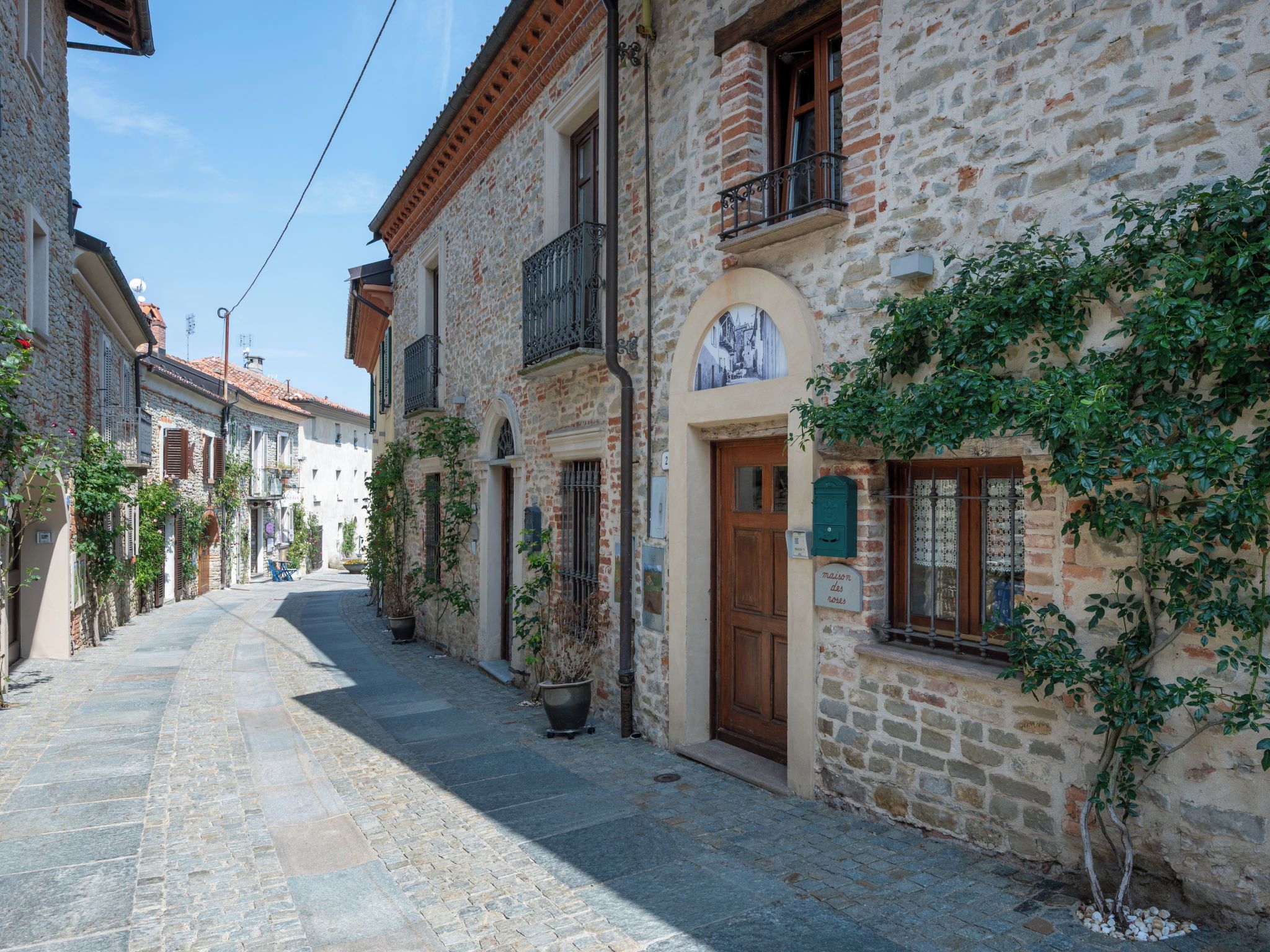 A narrow cobblestone street lined with historic stone buildings, some with balconies and potted plants.