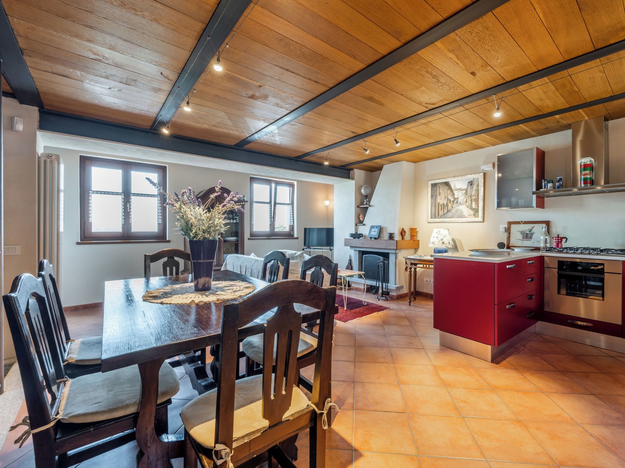 A dining area with a wooden table and chairs, a kitchen with red cabinets, and a painting on the wall.