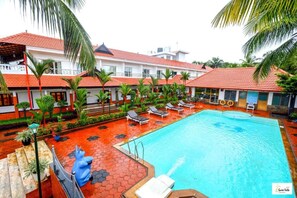 Hotel com piscina, palmeiras e telhados de telha vermelha.