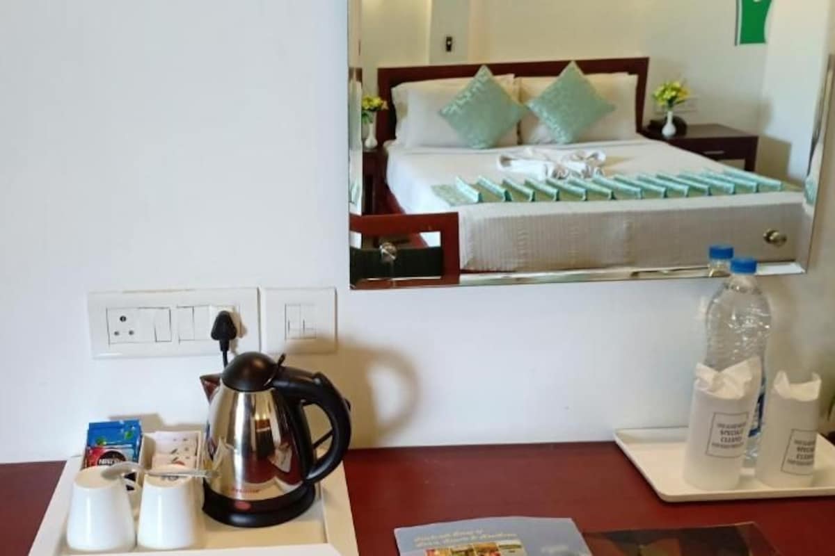 Een hotelkamer met een bed, een nachtkastje met een waterkoker, bekers en een fles water.