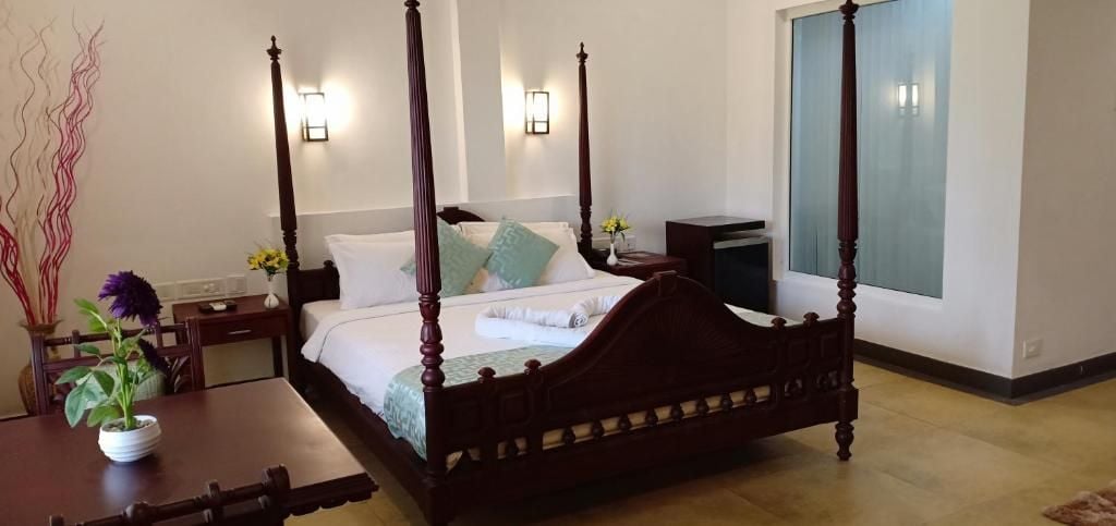 Uma cama de dossel com estrutura de madeira, uma mesa de cabeceira com abajur e um vaso com flores.