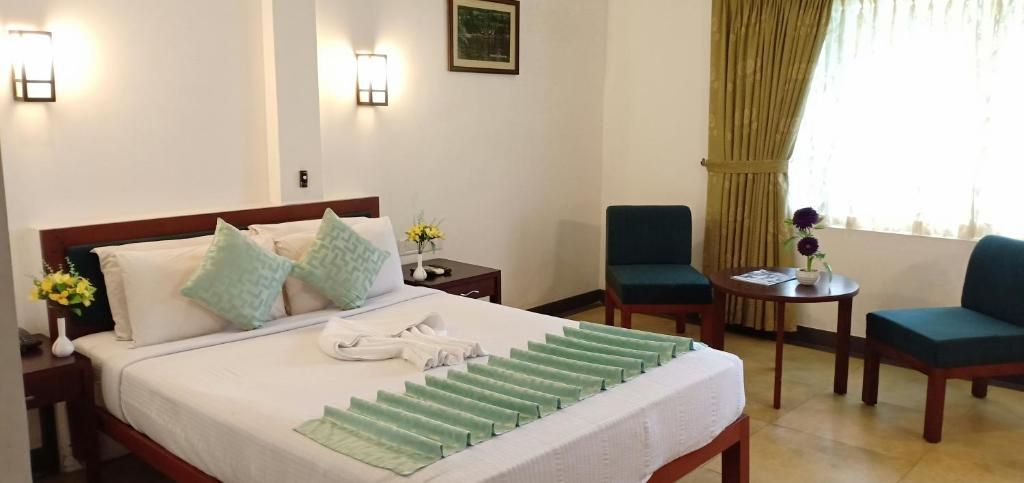 Una habitación de hotel con una cama, dos sillas, una mesita y un ventanal con cortinas.