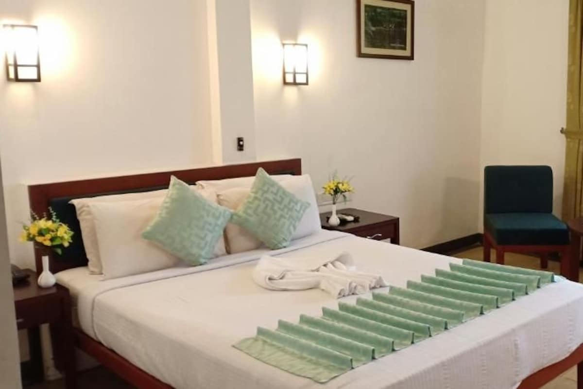 A hotel room with a bed, two chairs, a small table, and a window with curtains.