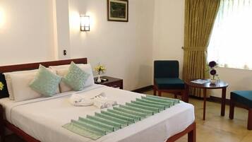 Una habitación de hotel con una cama, dos sillas, una mesita y un ventanal con cortinas.