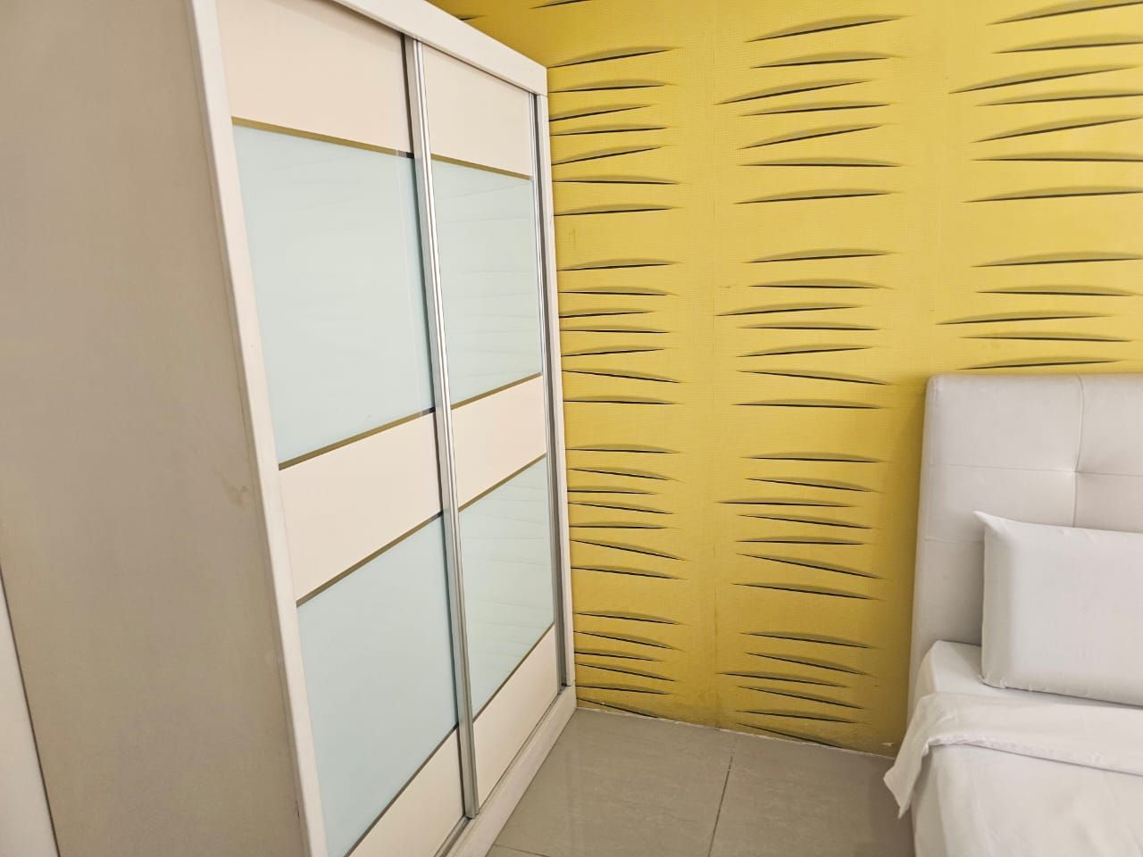 A room with a sliding wardrobe, a bed with white bedding, and a yellow textured wall.