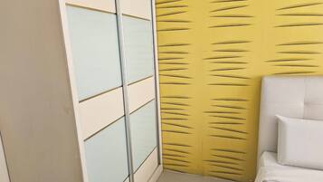 A room with a sliding wardrobe, a bed with white bedding, and a yellow textured wall.