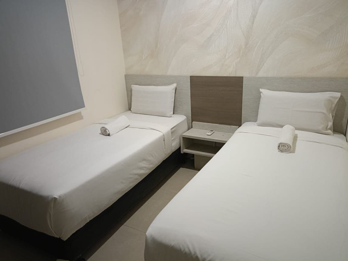 A hotel room with two single beds, a nightstand, and a wall-mounted TV.