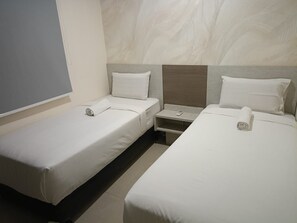 Habitación de hotel con dos camas individuales, una mesita de noche y un televisor montado en la pared.