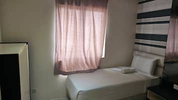 A single bed with a pillow, a bedside table, a window with curtains, and a wall with a striped pattern.