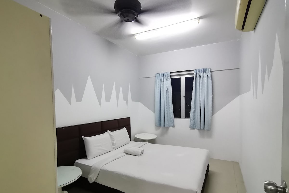 Una habitación de hotel con cama, una mesa redonda, ventana con cortinas y un ventilador de techo.