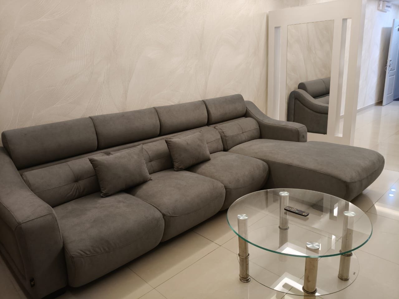 A grey sofa with a glass coffee table in a modern room with a tiled floor.