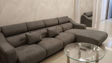 A grey sofa with a glass coffee table in a modern room with a tiled floor.
